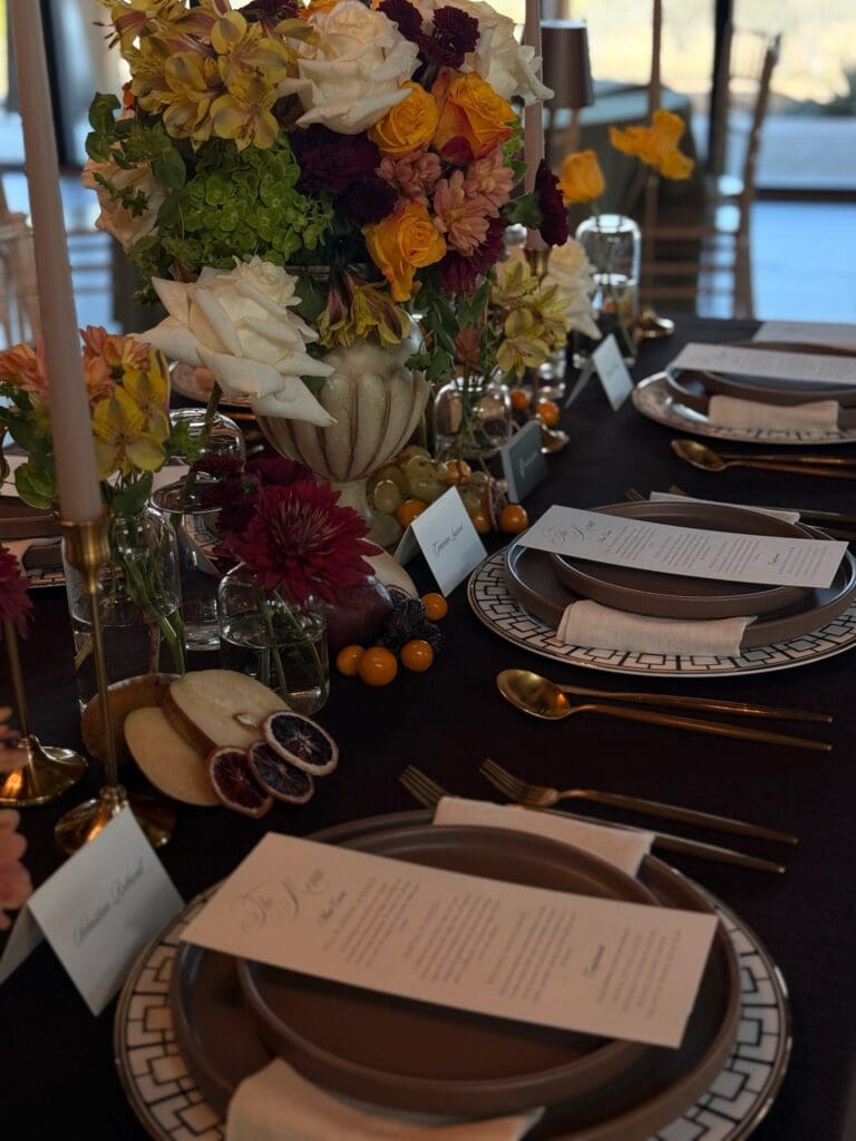 Angled close-up of a Dutch Masters inspired wedding centerpiece featuring mustard roses, deep burgundy mums, and sliced fruit accents styling by Austin wedding planner Olive & Eden.