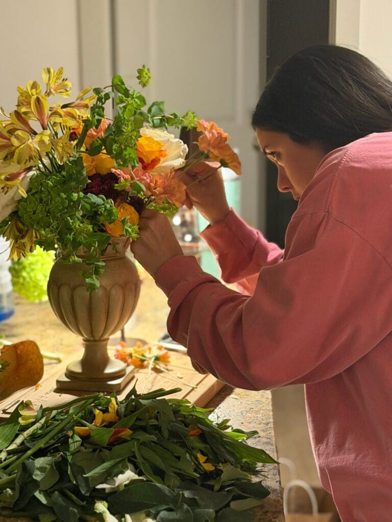 Olive & Eden founder Lauren placing a burgundy flower into a vintage vase during a wedding design styling session.