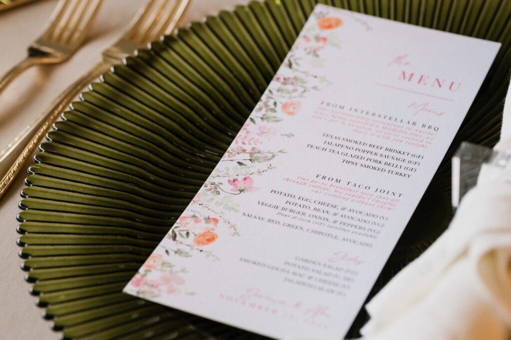 Close-up of a custom-designed floral wedding menu by Olive & Eden featuring Interstellar BBQ and Taco Joint storytelling.