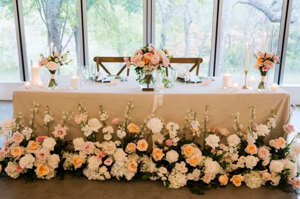 A "flower meadow" floral installation lining the front of a wedding head table with oatmeal velvet linens.