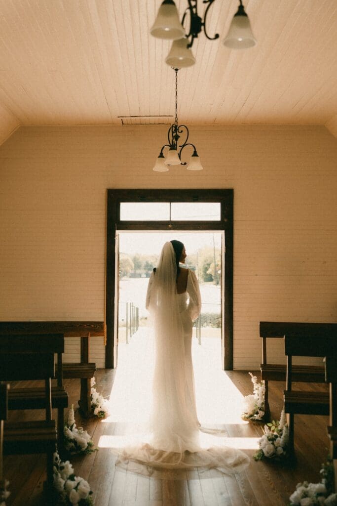 A cinematic silhouette of a bride standing in the light of the historic Hill Country Wedding Chapel doorway in Fredericksburg, Texas.