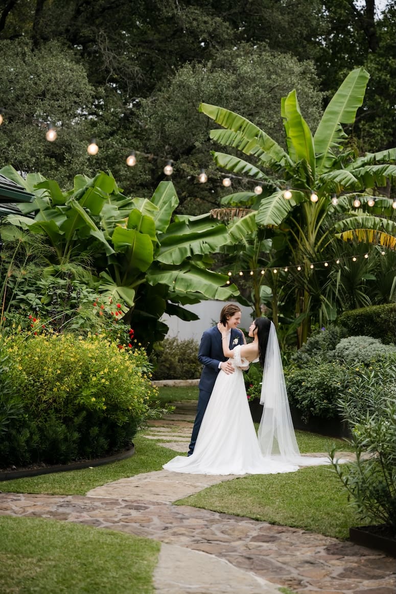 A romantic garden wedding portrait at Hummingbird House designed by Austin wedding planner Olive & Eden, featuring a bride and groom on a stone path under bistro lights.